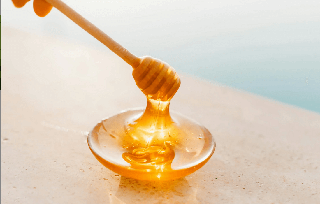 A close-up image of a honey stick with a rounded end, dripping golden honey.